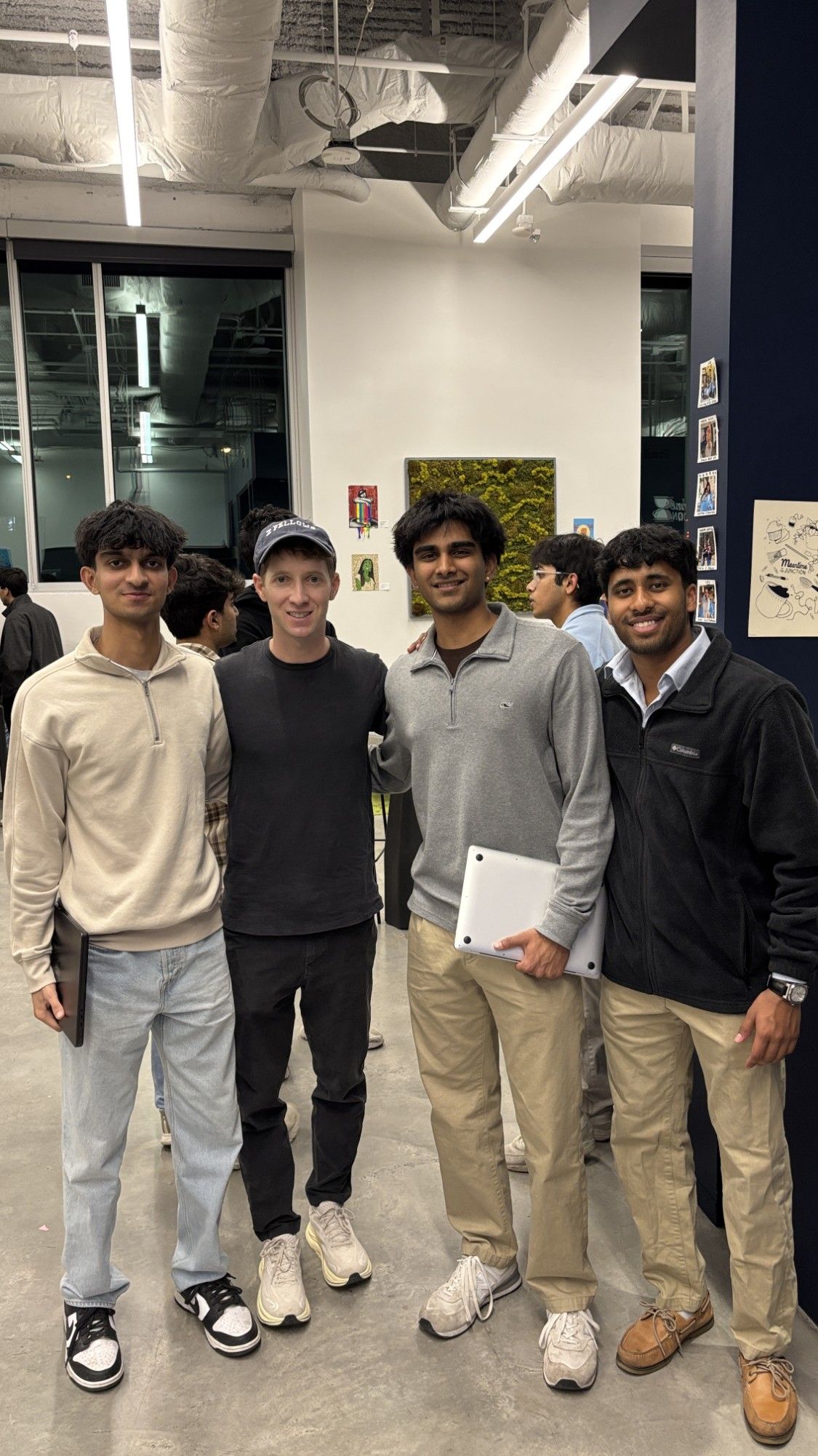 Four people standing side by side at an indoor event, two of them holding laptops.