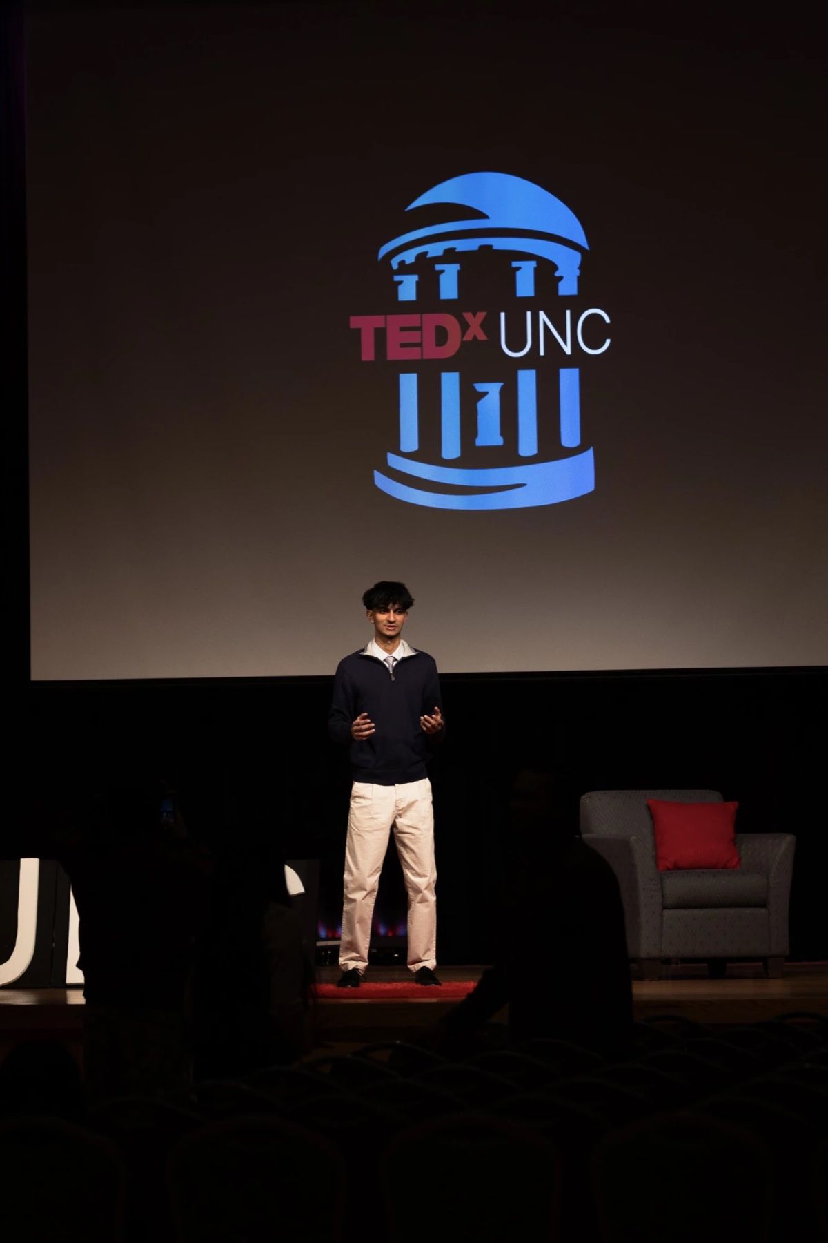 Jason speaking on stage at TEDxUNC, with the TEDxUNC logo on the screen behind him.
